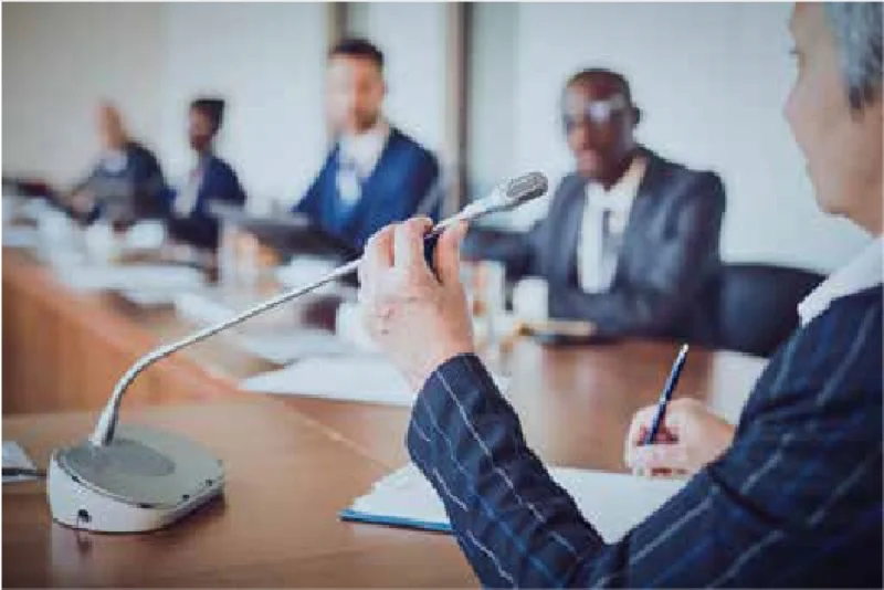 Executives around a boardroom table, one of them speaking into a microphone