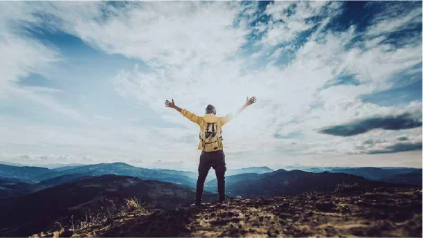 A climber with arms raised on a mountain ridge